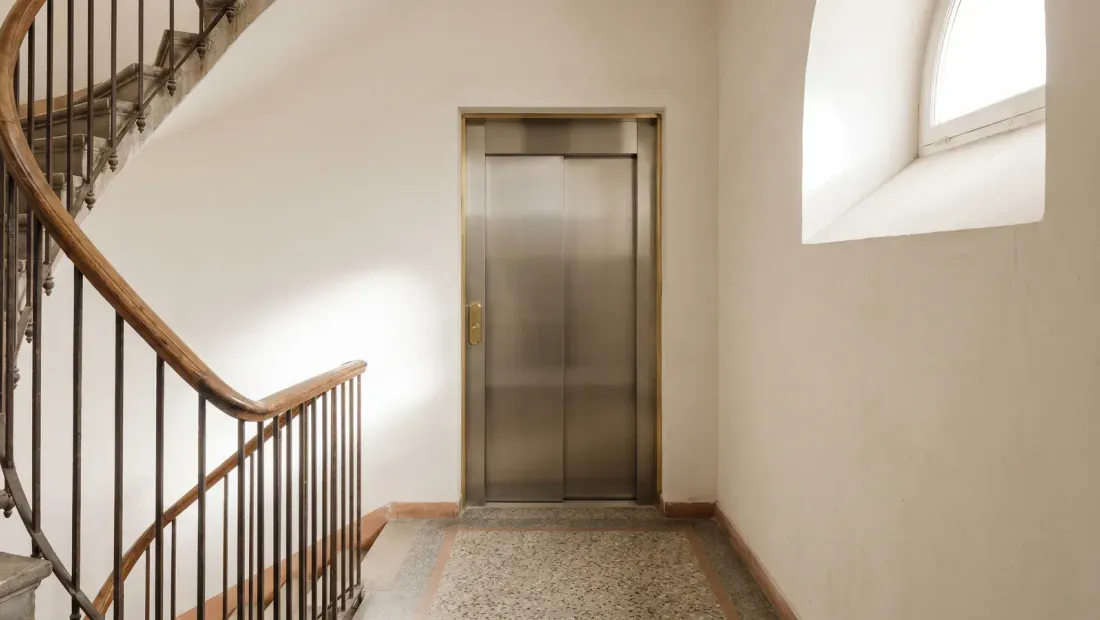 Pasillo interior de edificio residencial español con ascensor y escalera, ilustrativo de la STS 2920/2025 sobre exención de cuotas del ascensor en comunidades de propietarios