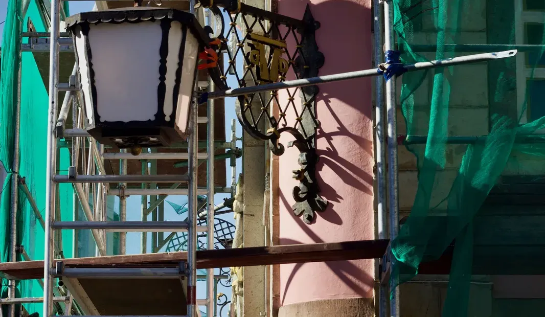 Edificio en rehabilitación de fachada con andamio y malla verde de protección (Plan Rehabilita Madrid 2026)